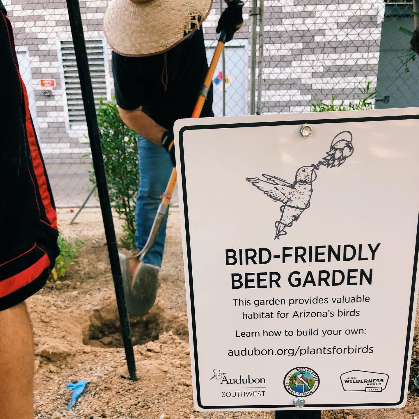 Bird Friendly Beer Garden sign with volunteers planting native plants in the background.