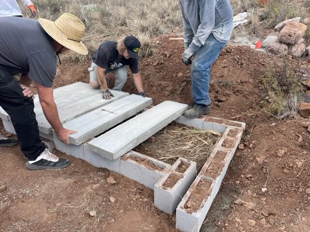 Surrounded by vast desert grasslands, a group of volunteers lay large concerete slabs atop a rectangular frame made of gray cinder blocks.