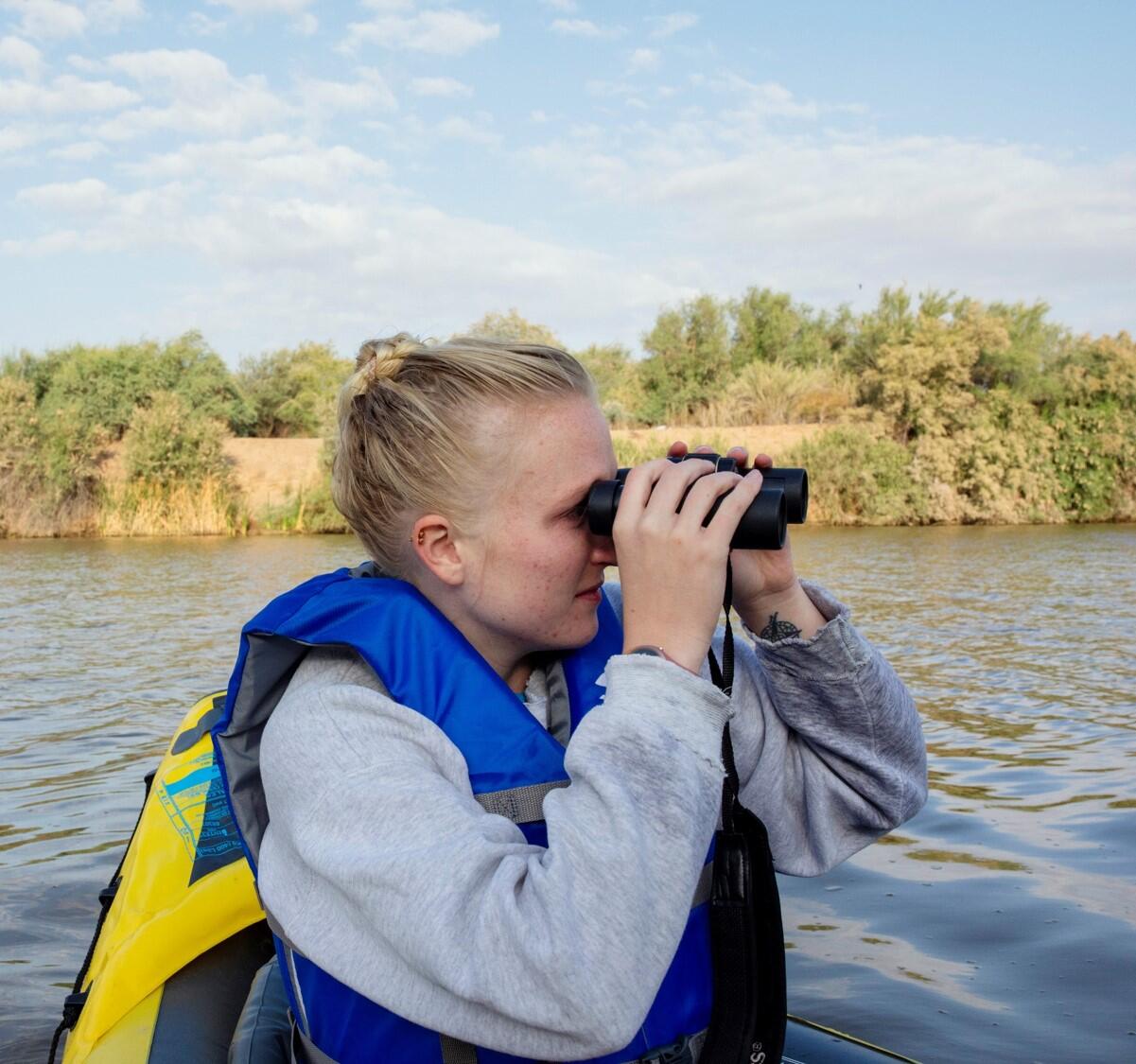 Emma Laurens scopes out a bird with her binoculars in a kayak while surveying for marsh birds on the Gillespie Dam.