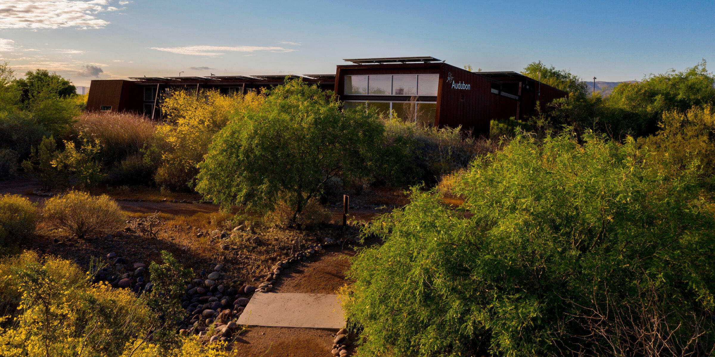 The Rio Salado Audubon Center, a rusted crimson building nestled amidst blooming desert foliage in Phoenix, Arizona.